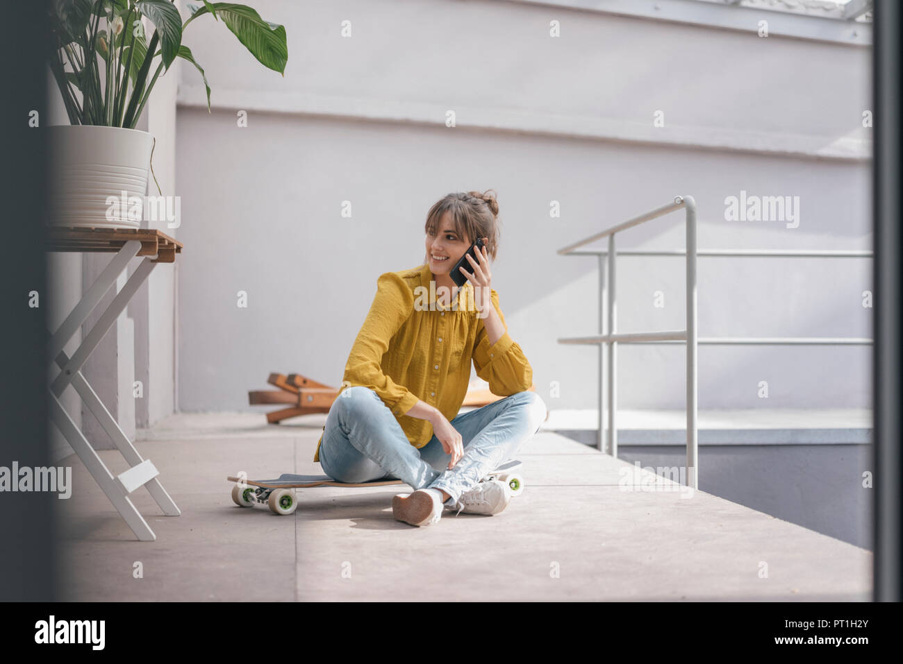 Young woman sitting on skateboard, using smartphone Stock Photo