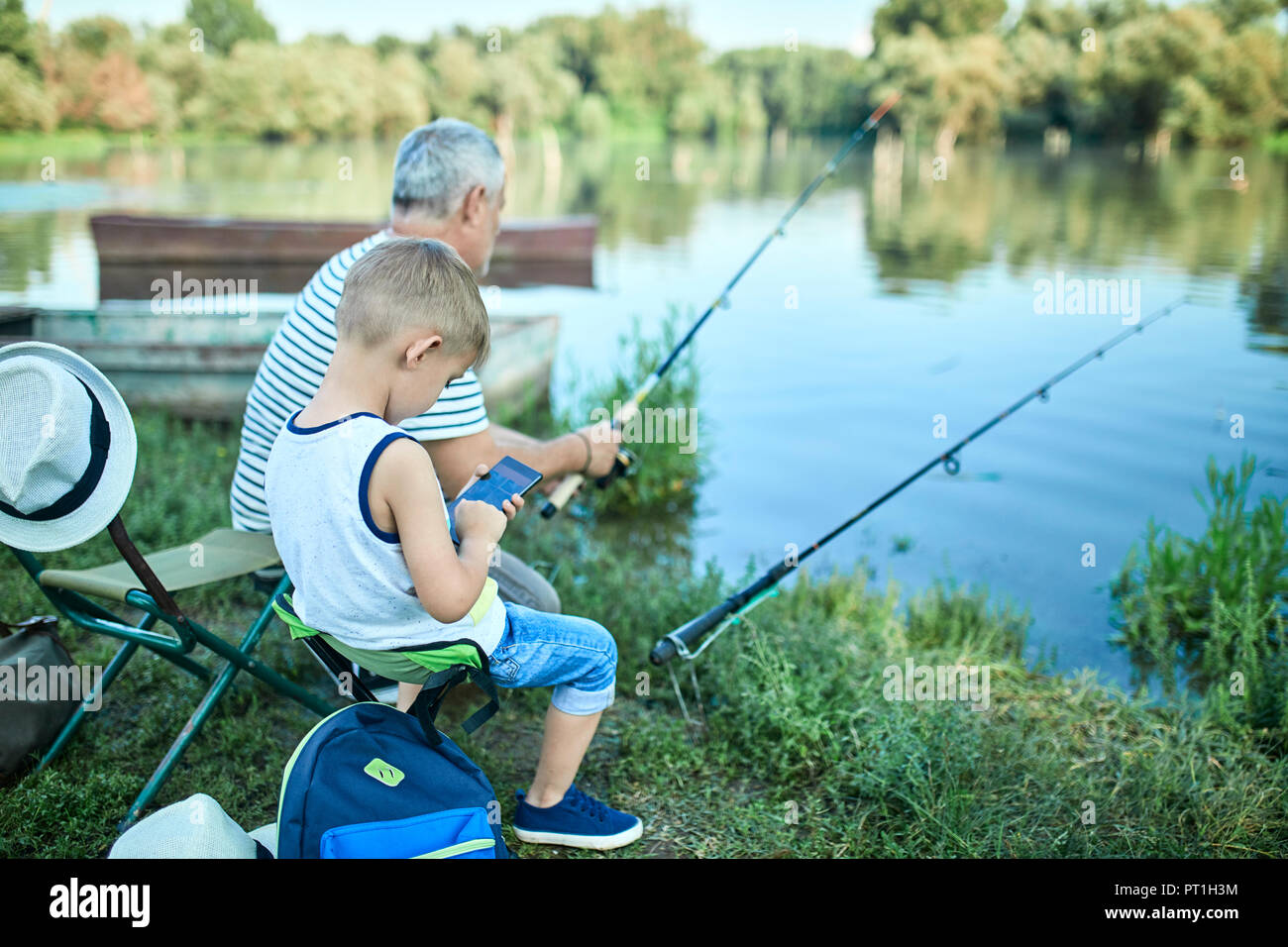Little boy sitting with grandfather at lakeshore testing smartphone Stock Photo