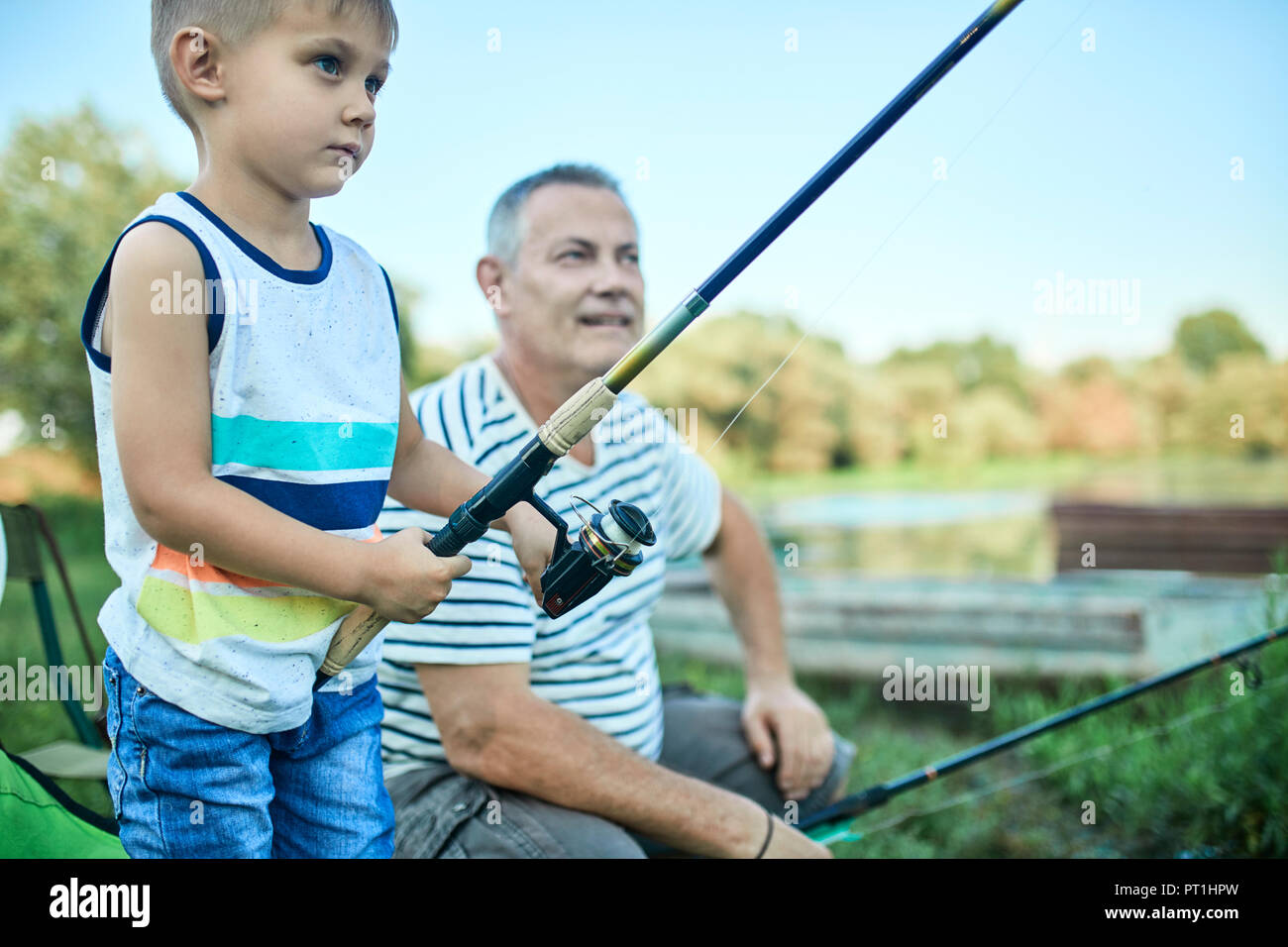 Little boy fishing together with his grandfather at lakeshore Stock Photo