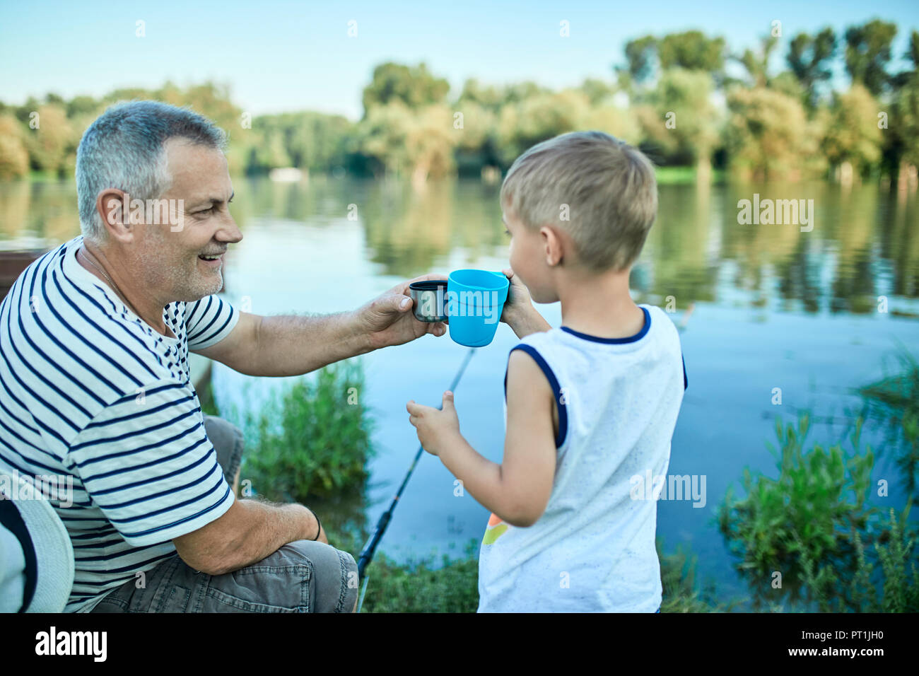 Grandfather and grandson toasting together at lakeshore Stock Photo