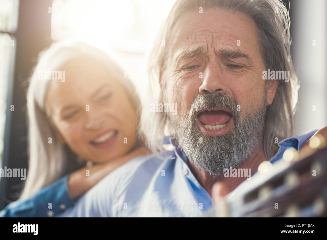 Senior playing guitar and singing loud for his wife Stock Photo