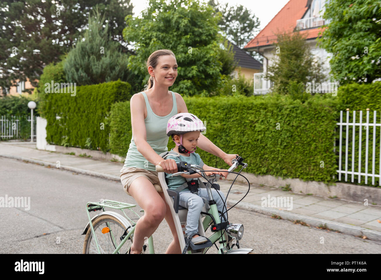 Mother and daughter riding bicycle, daughter wearing helmet sitting in children's seat Stock Photo