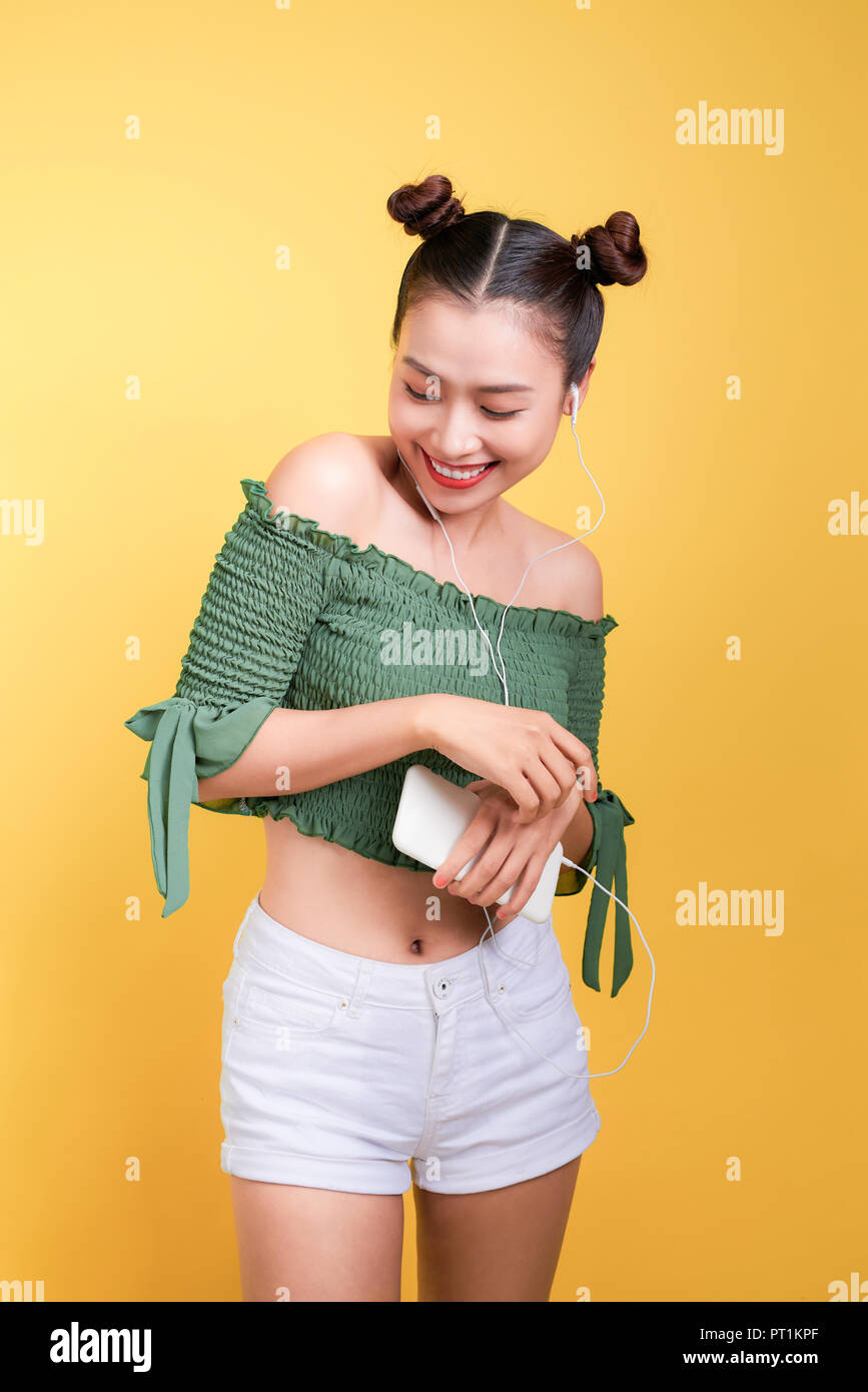 Fashion smiling asian woman listening to music in earphones over yellow ...