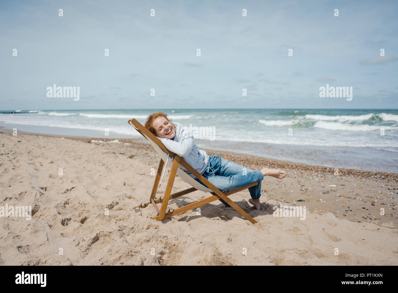 Smiling woman lying in deck chair, enjoying sunbath at the beach Stock Photo