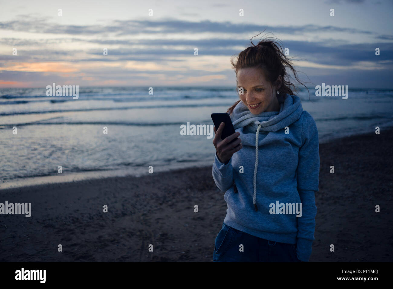 Woman using smartphone on the beach at sunset Stock Photo
