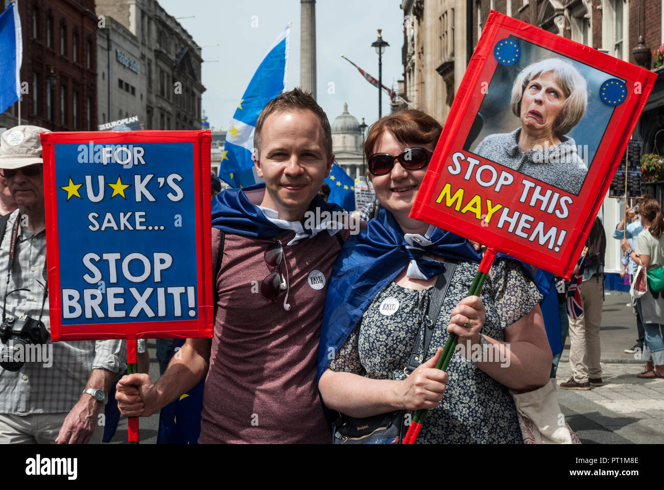 Young smiling couple holding humorous placards 'For *U*KS sake stop Brexit', 'Stop this Mayhem' with a gurning picture of Teresa May. Stock Photo