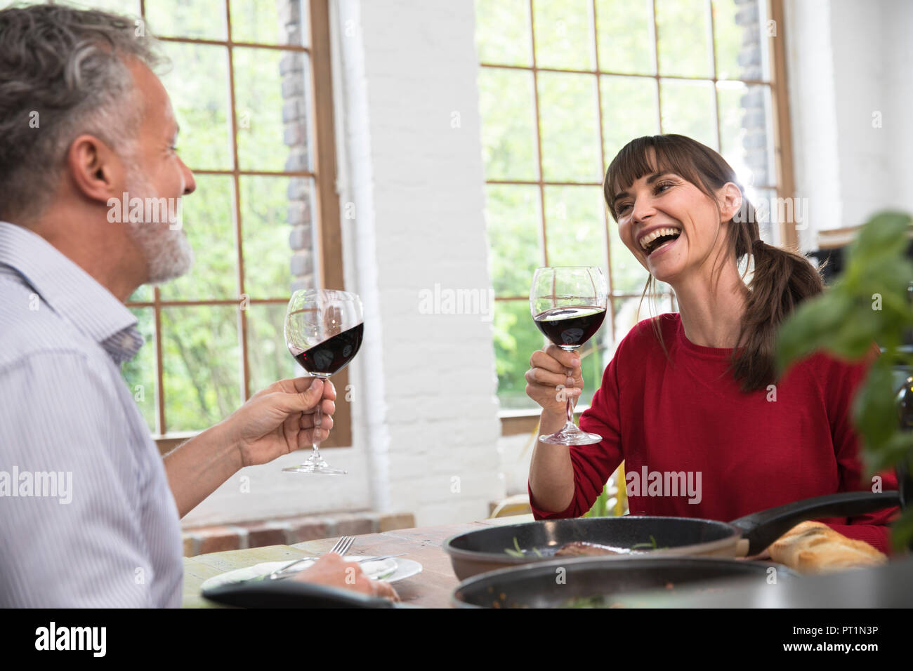 Happy couple sitting in kitchen, toasting with red wine, enjoying dinner Stock Photo