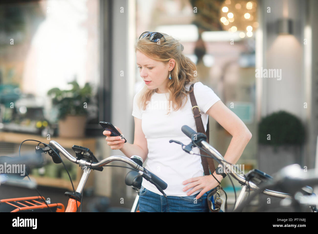 Germany, young woman with smartphone renting a city bike Stock Photo