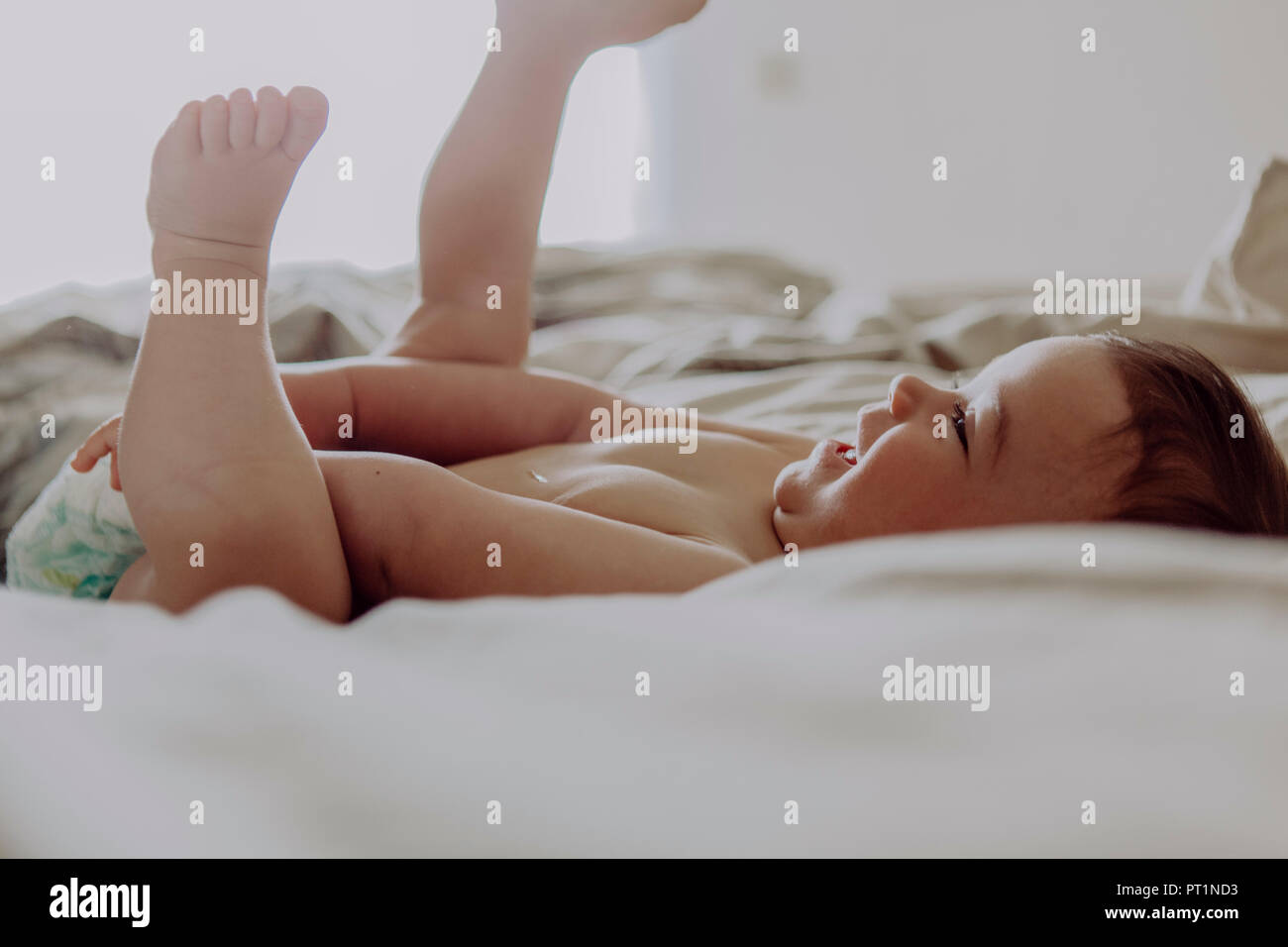 Happy baby, lying on bed, laughing Stock Photo