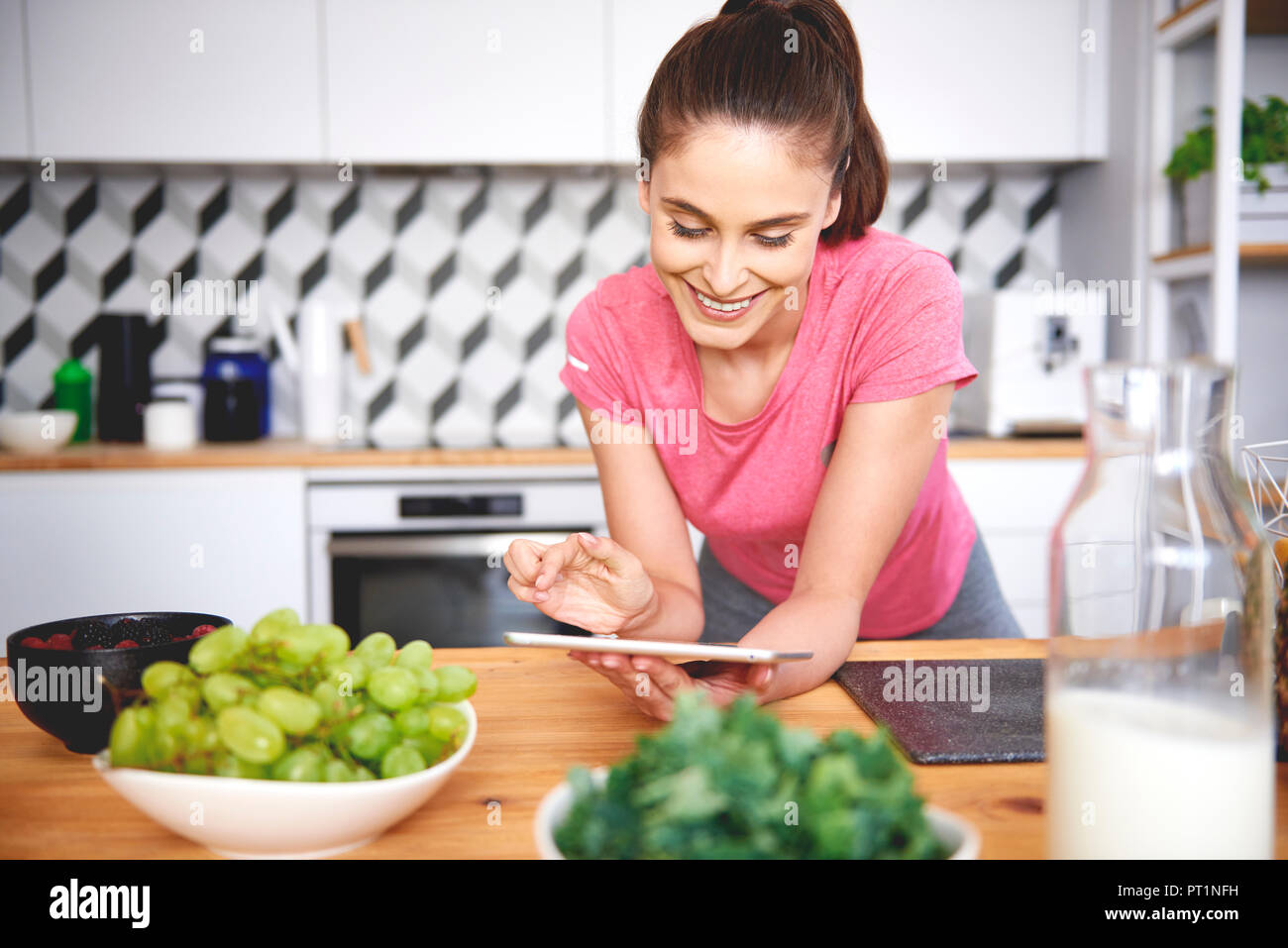 Smiling young woman using tablet in the kitchen Stock Photo