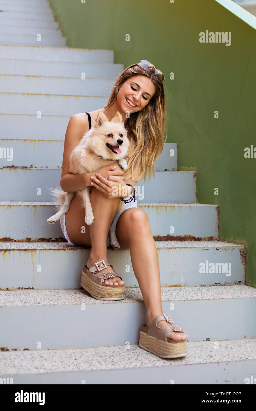 Smiling young woman sitting on stairs, holding her dog Stock Photo