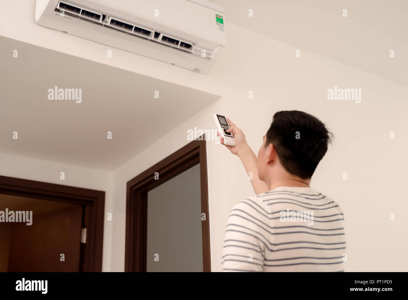 Young man switching on or adjusting the wall mounted air conditioner in the living room with a remote control Stock Photo