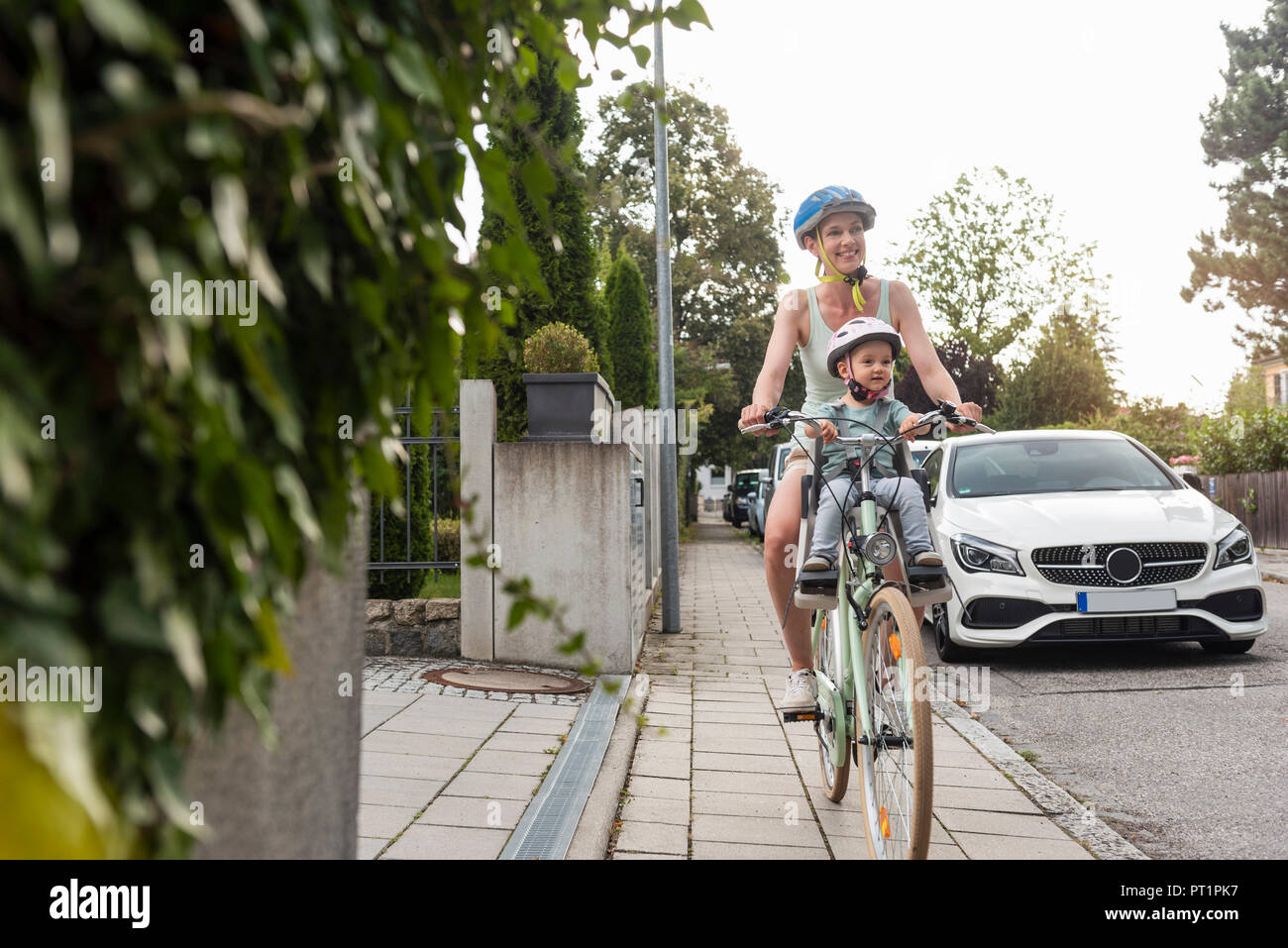 Mother and daughter riding bicycle, daughter wearing helmet sitting in children's seat Stock Photo