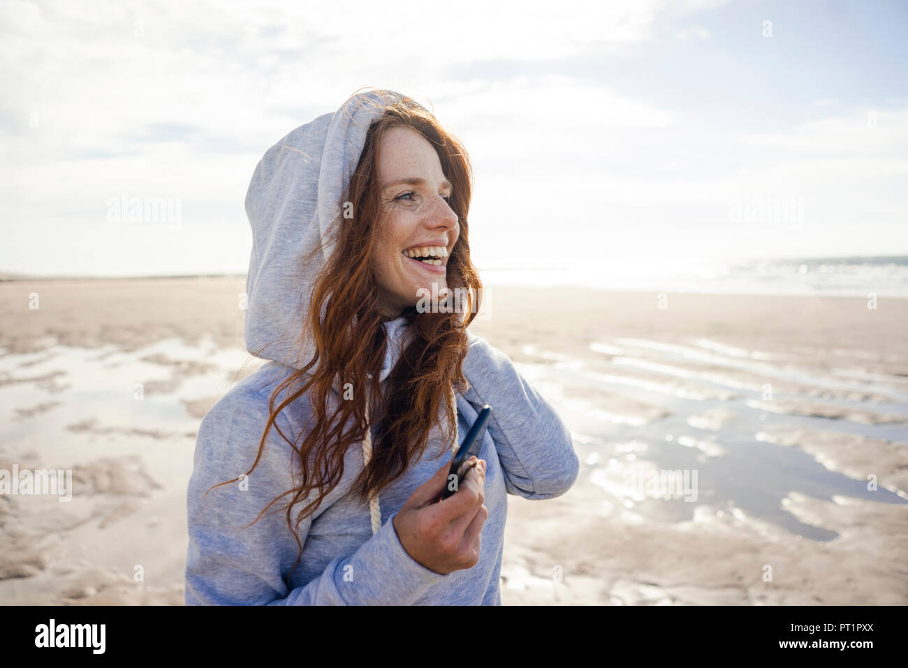 Woman having fun on a windy beach, wearing hood Stock Photo