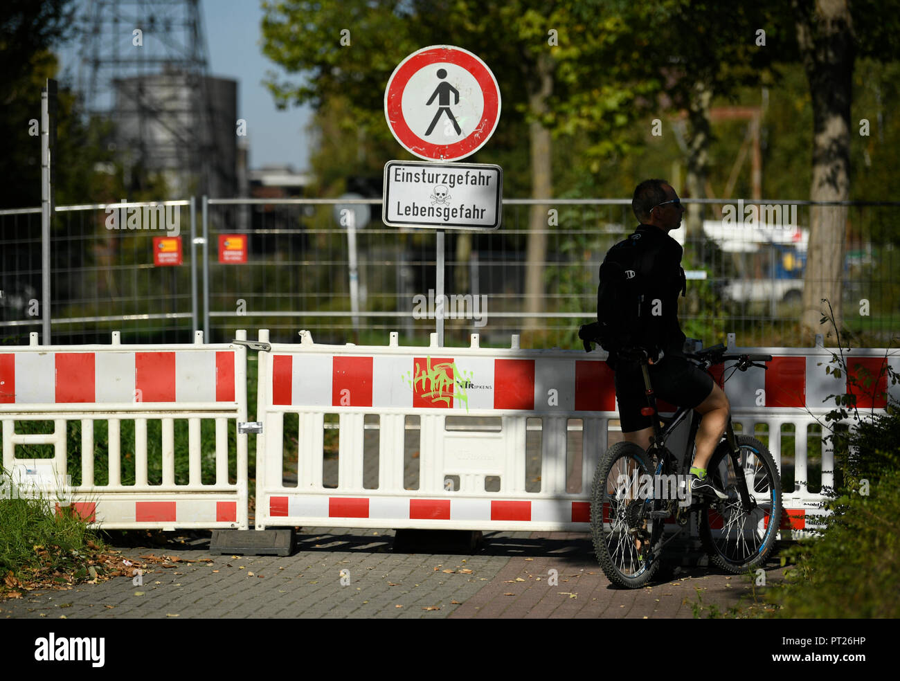 06 October 2018, North Rhine-Westphalia, Dortmund: A cyclist standing in front of a barrier along the sunken Emscherallee in the Huckarde district. The road continued to sag yesterday for several meters and is now closed for 150 meters. A large detour has been set up. Photo: Ina Fassbender/dpa Stock Photo