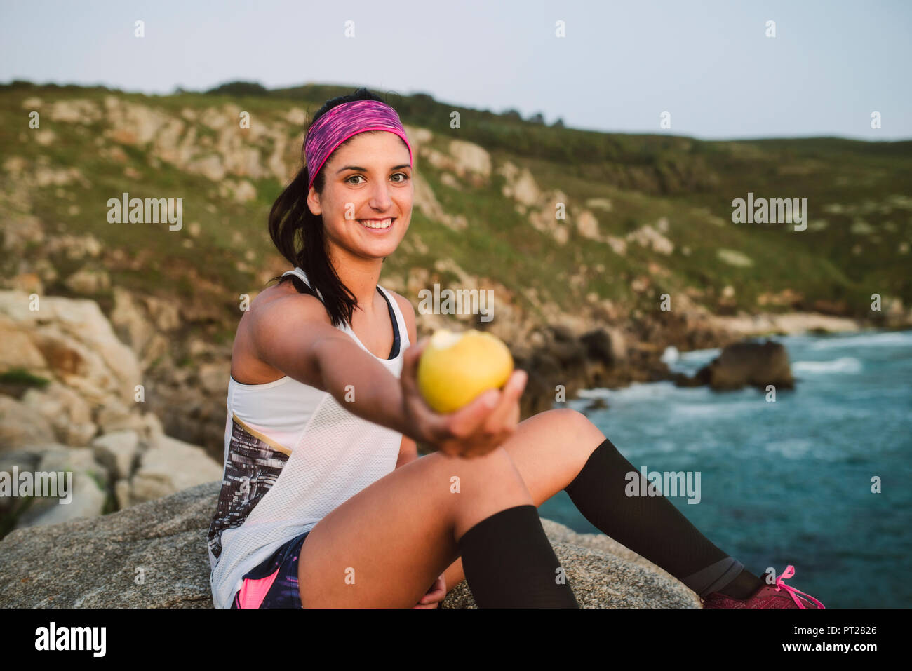 Sportive woman sitting on rocks, holding apple Stock Photo