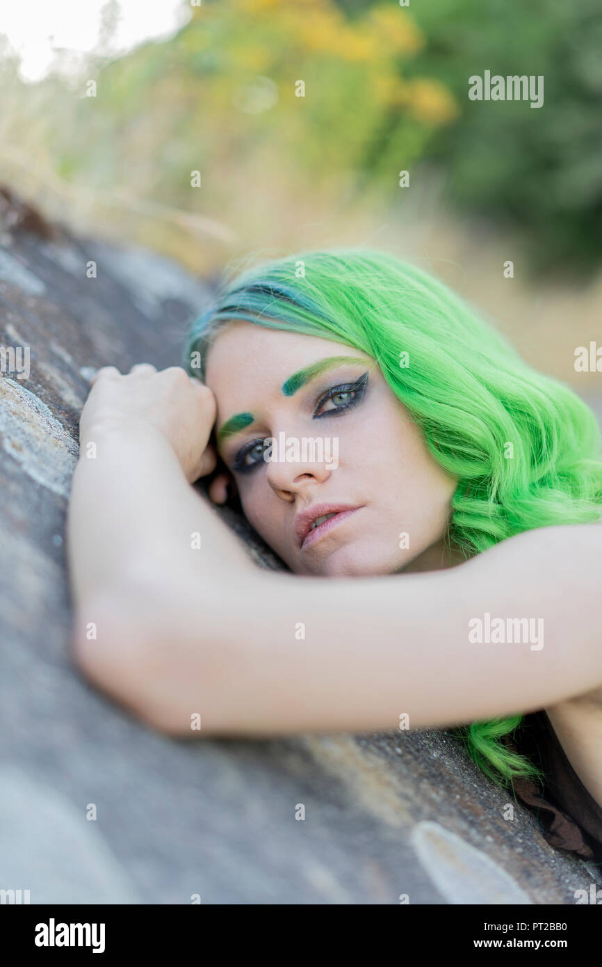 Portrait of young woman with dyed green hair and eyebrows in nature ...