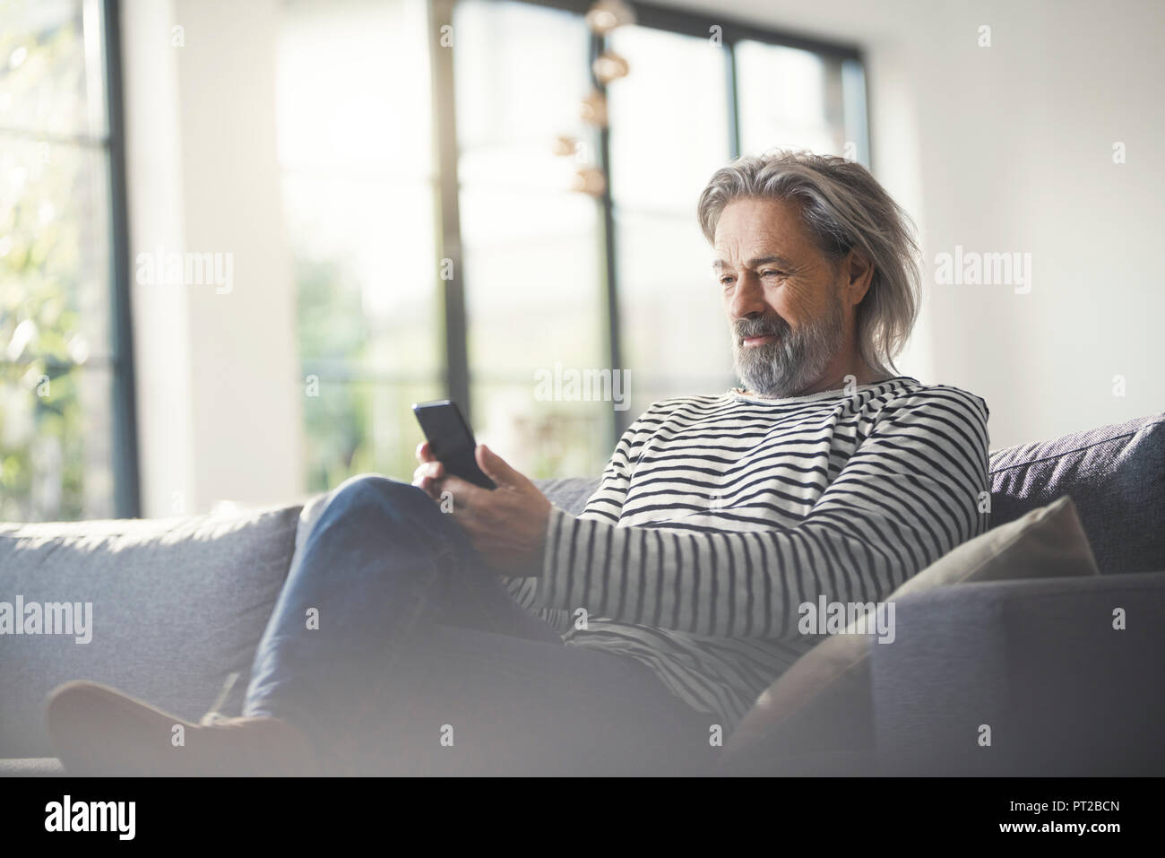 Senior man sitting on couch, using smartphone Stock Photo