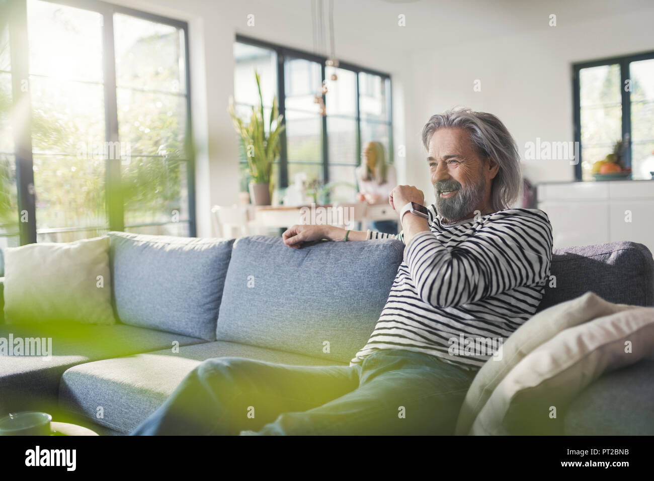 Senior man sitting on couch, talking into smartwatch Stock Photo