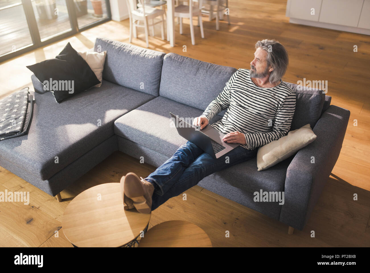 Senior man sitting on couch, using laptop Stock Photo