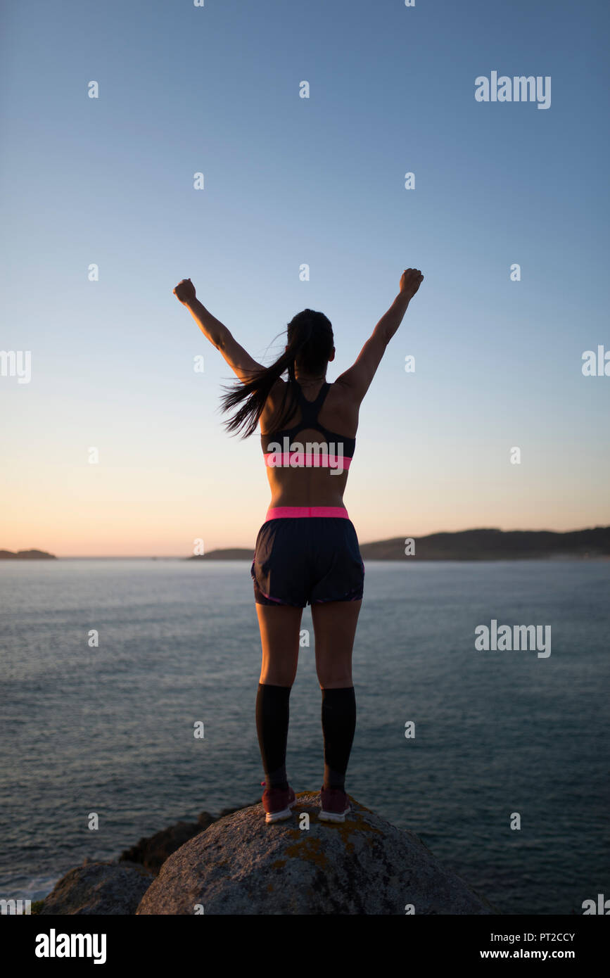 Woman with arms raised in front of a coastal landscape Stock Photo