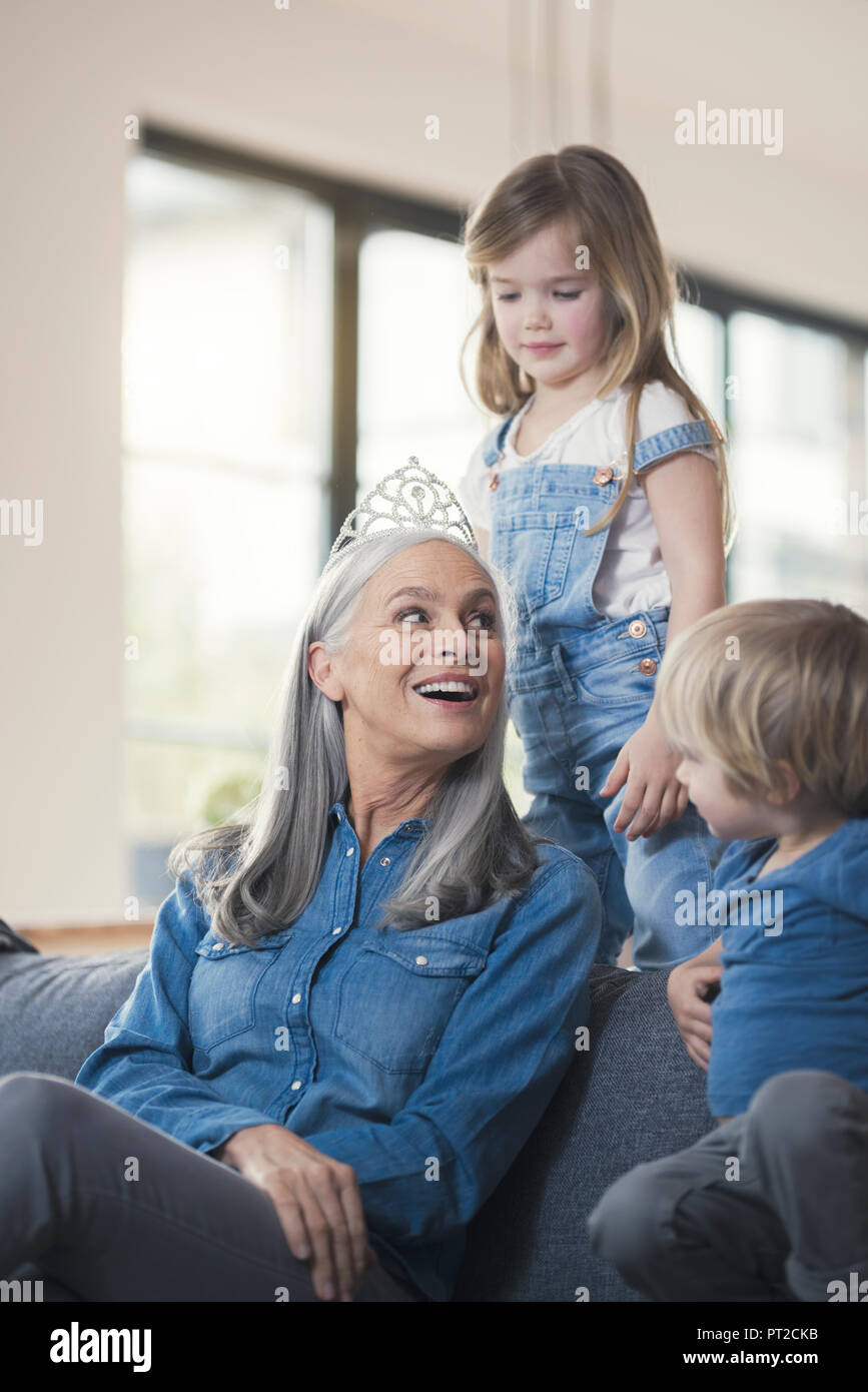 Grandmother wearing crown, sitting on couch with grandchildren Stock Photo