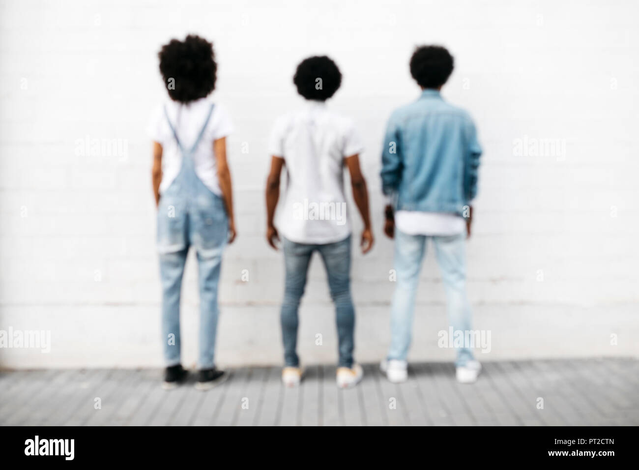 Back view of three friends standing side by side in front of white wall ...