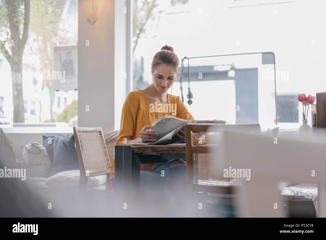 Young woman sitting in coworking space, reading newspaper Stock Photo