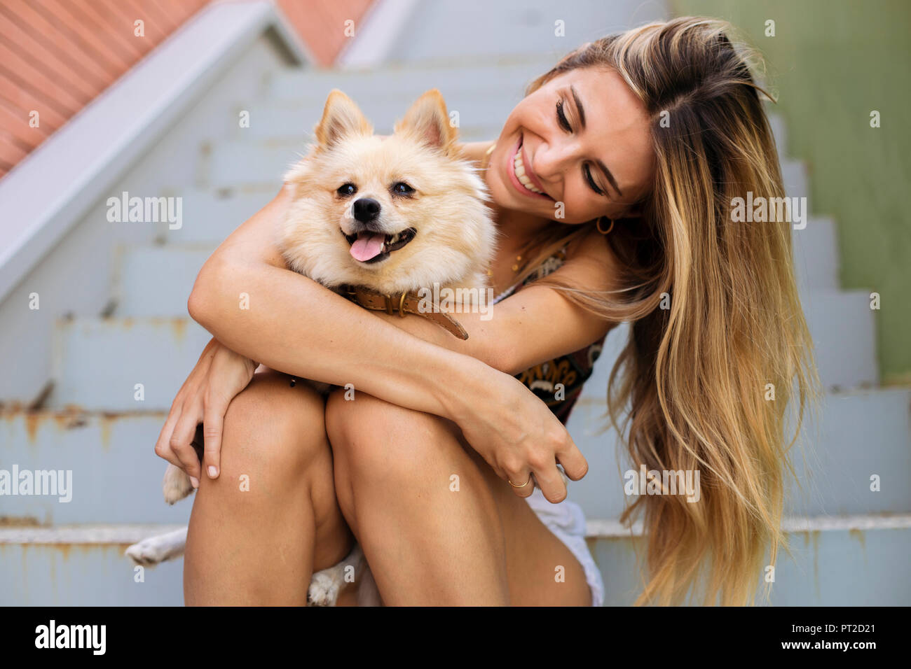 Smiling young woman sitting on stairs holding her dog Stock Photo