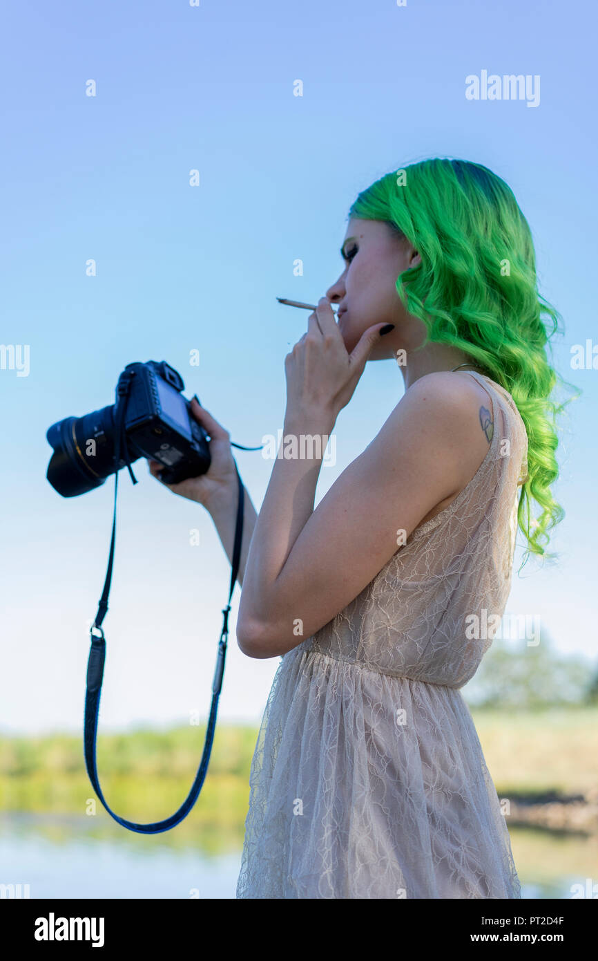 can you smoke a cigarette with hair dye in Young woman with dyed green hair smoking cigarette in nature while looking  at display of digital camera Stock Photo