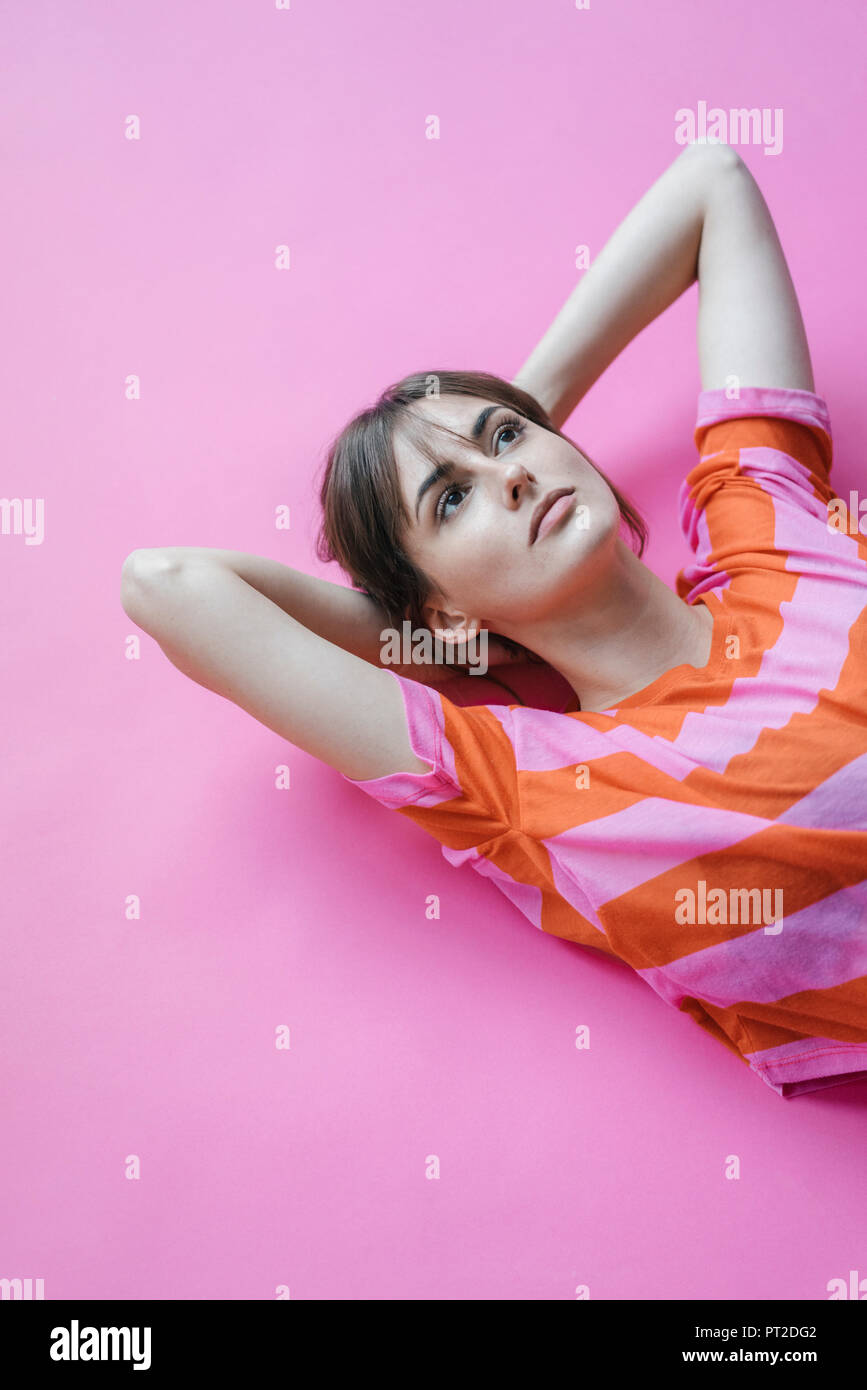 Woman lying on pink background with hands behind head, thinking Stock Photo