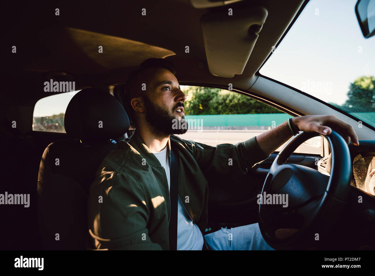 Bearded young man looking at rear-view mirror while driving car Stock Photo