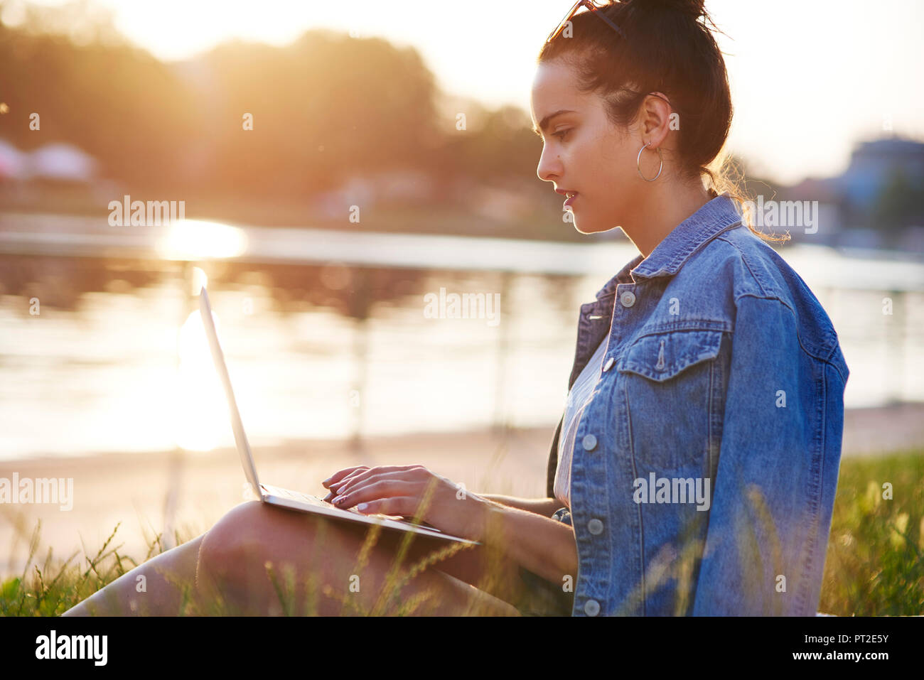 Young woman sitting on a meadow at evening twilight using laptop Stock Photo