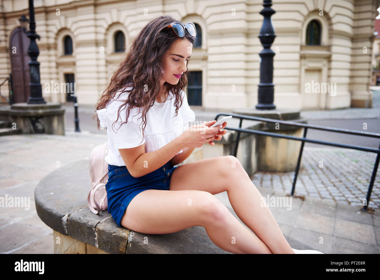 Young woman sitting on a wall using cell phone Stock Photo