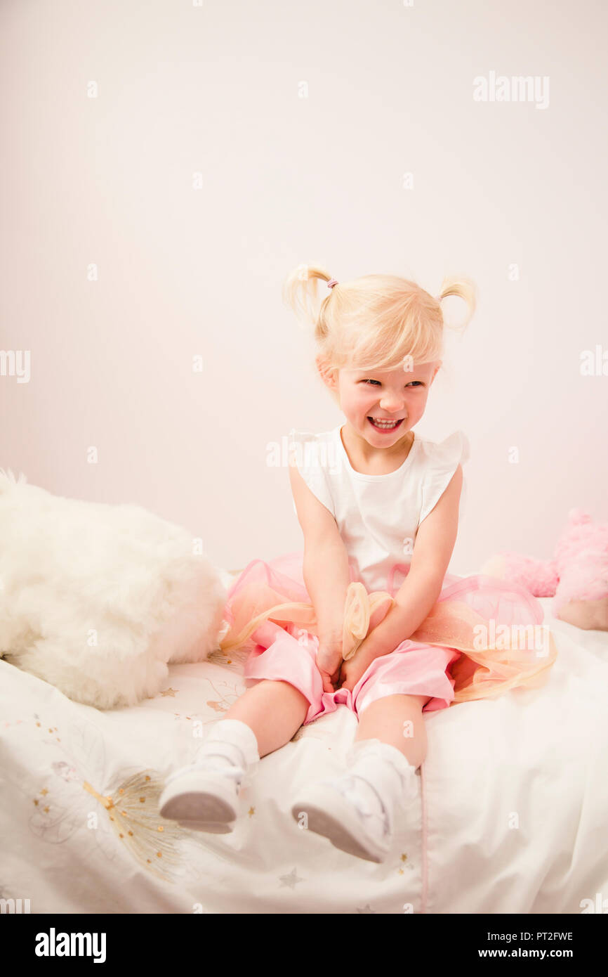 Portrait of laughing little girl sitting on bed Stock Photo