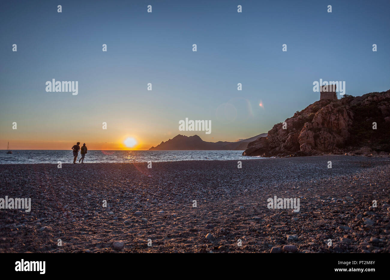 2 people on the beach in front of atmospheric sunset Stock Photo