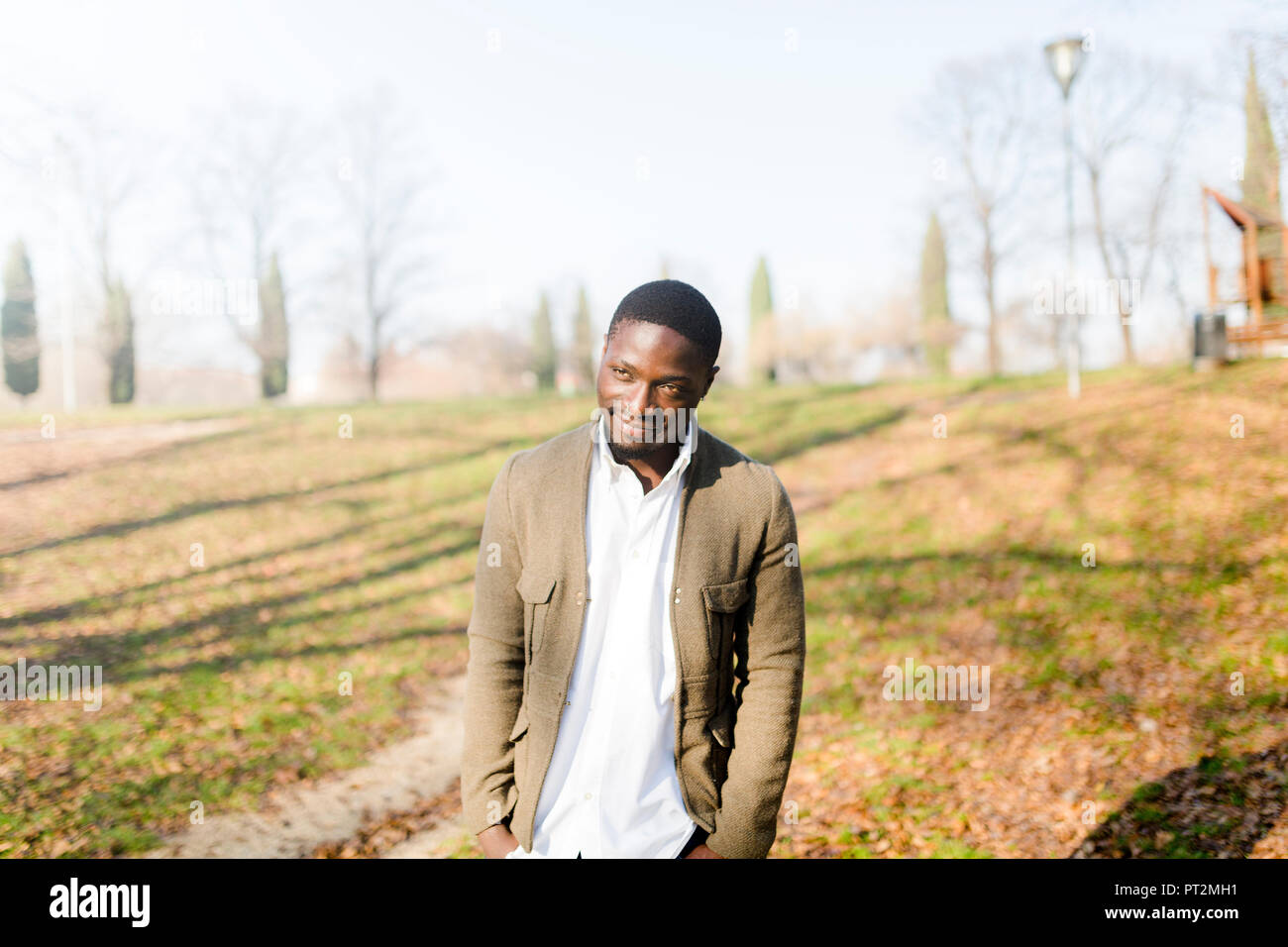 Portrait ogf young man in park, wearing jacket, looking shy Stock Photo