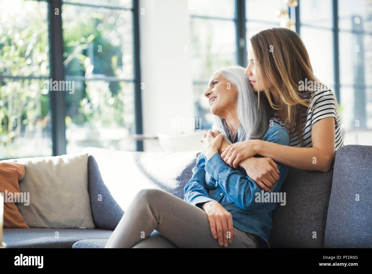 Daughter holding mother in her arms, sitting on couch Stock Photo