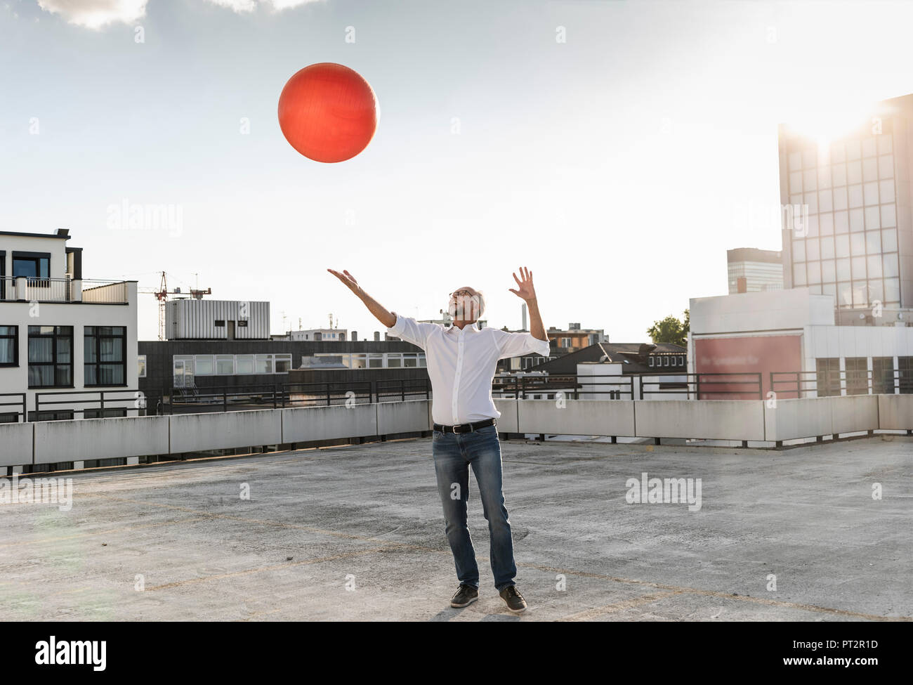 Mature man playing with orange fitness ball on rooftop of a high-rise building Stock Photo