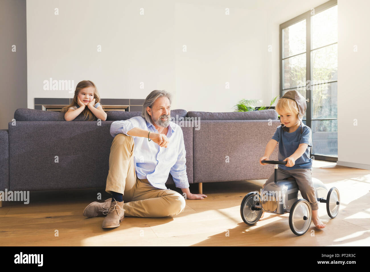 Grandfather playing with grandchildren, sitting on toy car Stock Photo
