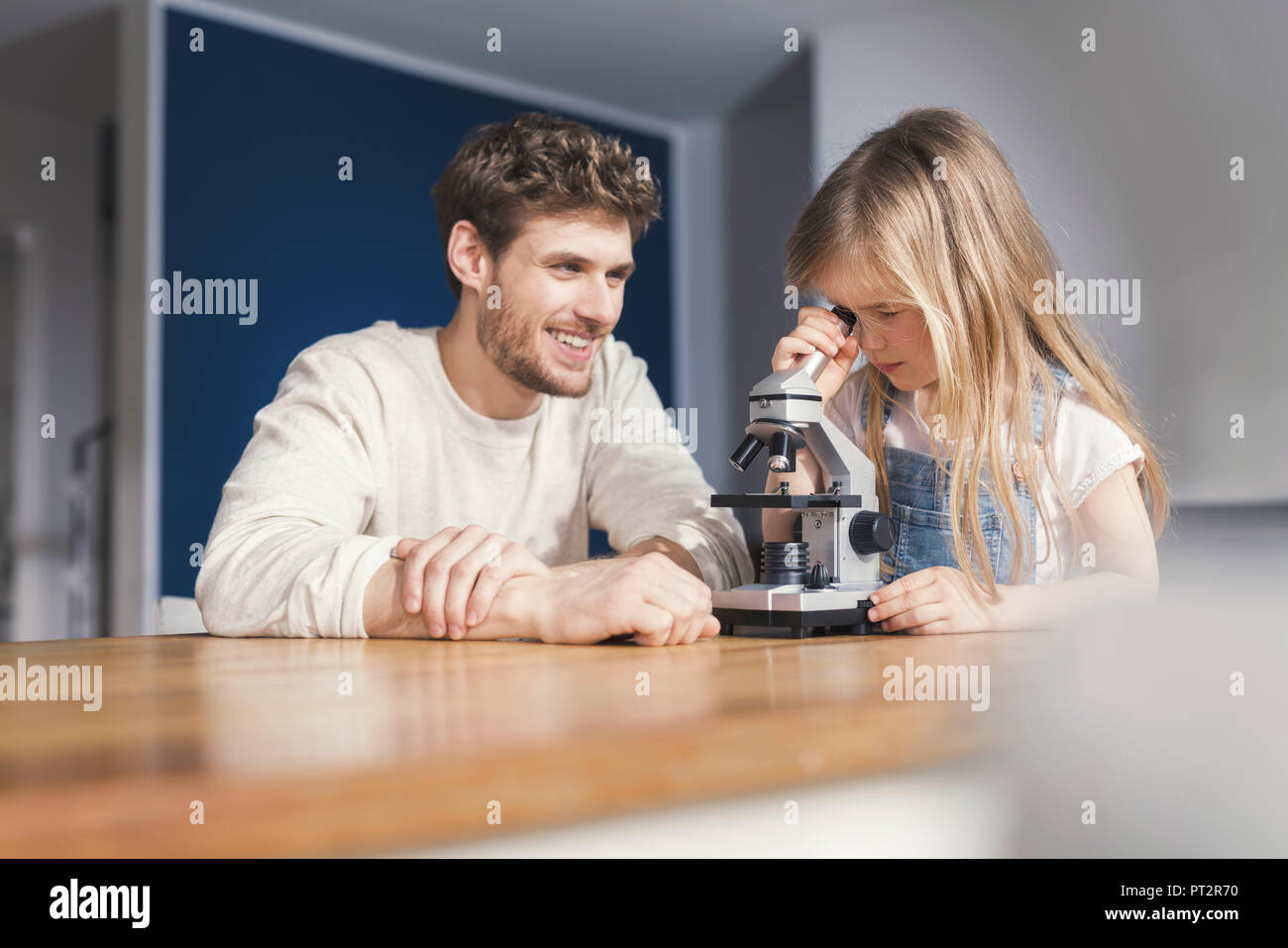 Father watching daughter use a microscope, smiling proudly Stock Photo