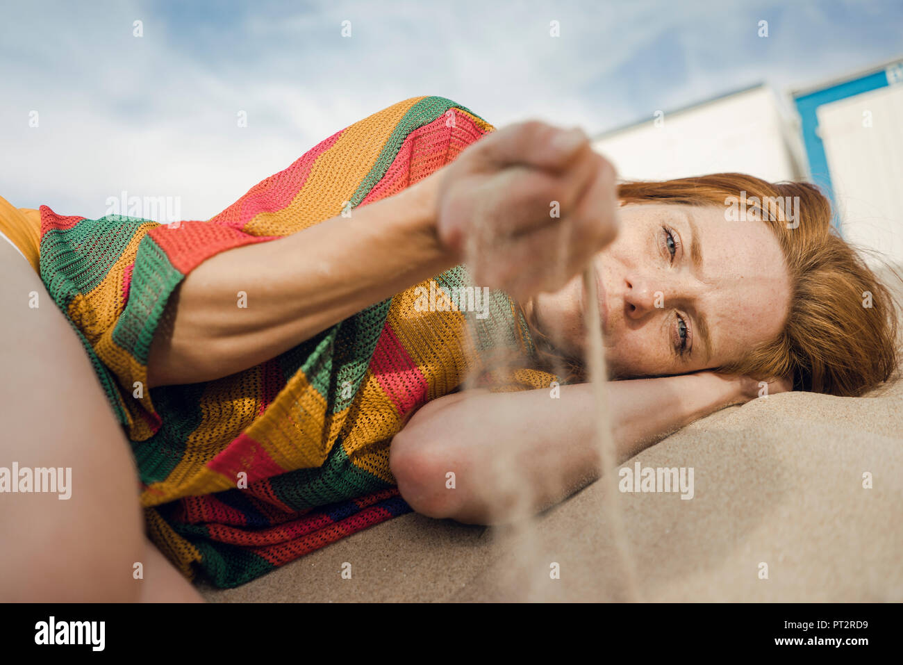 Redheaded woman lying on the beach, with sand trickling through her hand Stock Photo