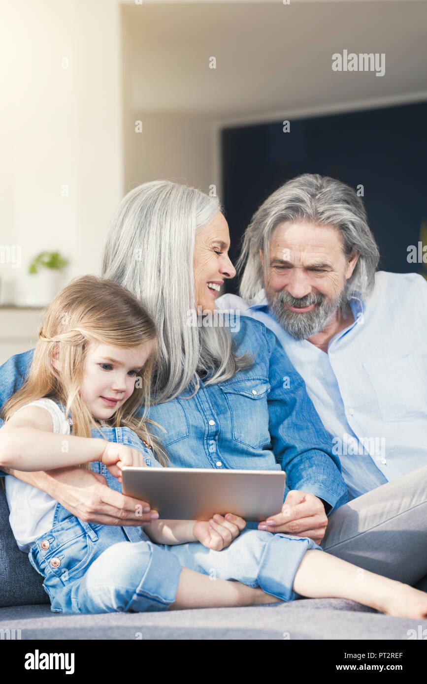 Grandparents and granddaughter sitting on couch, using tablet Stock Photo