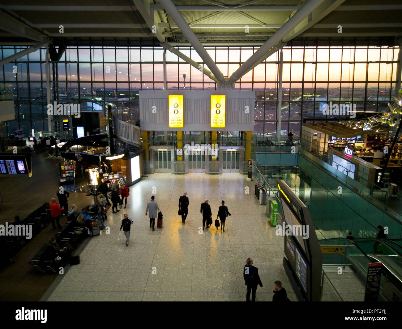 Terminal 5, London Heathrow Airport at sunrise as seen from balustrade with travelers and waiting area Stock Photo
