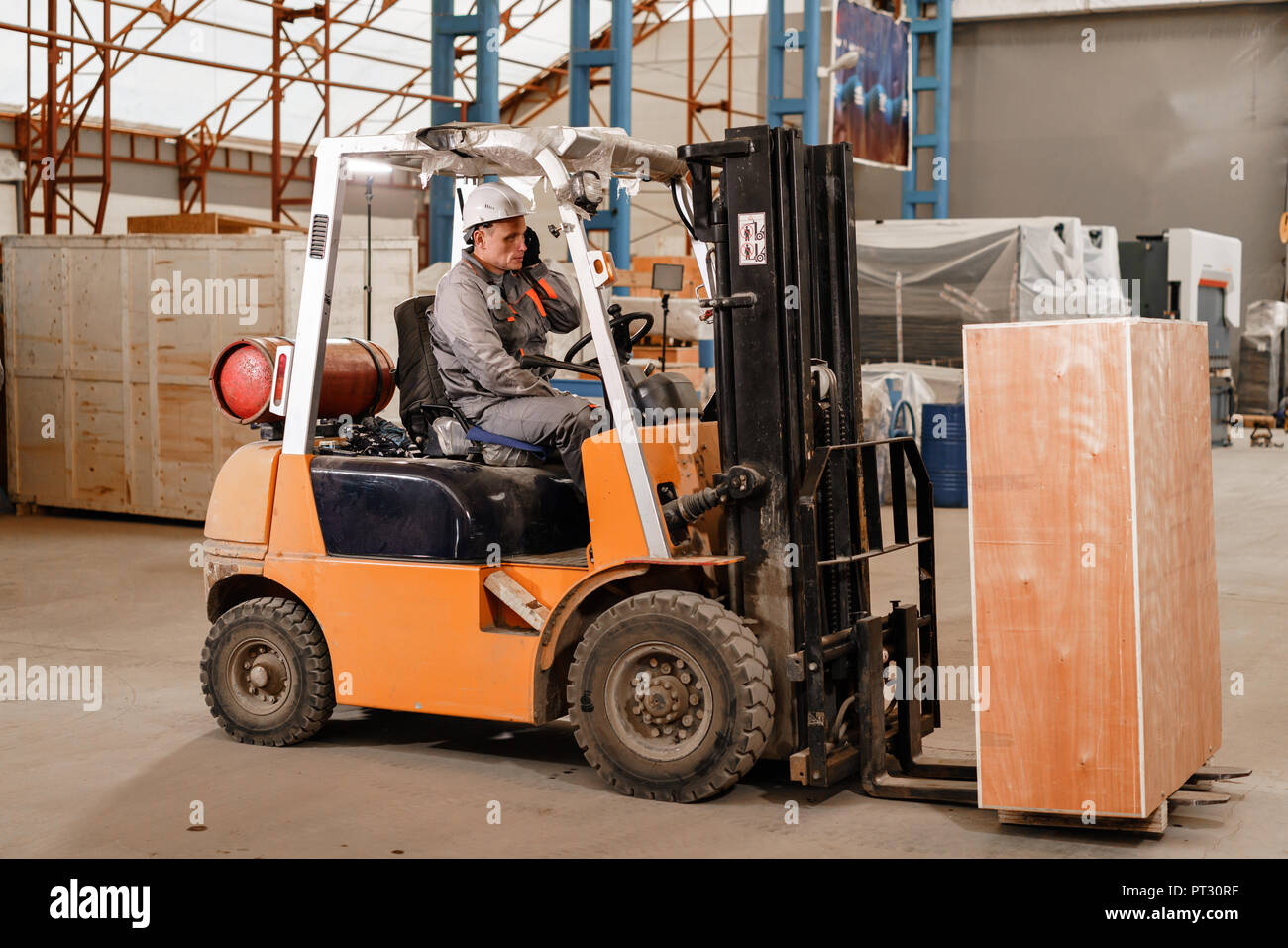 man driving a forklift through a warehouse in a factory. driver in uniform and protective helmet. the concept of logistics and storage Stock Photo