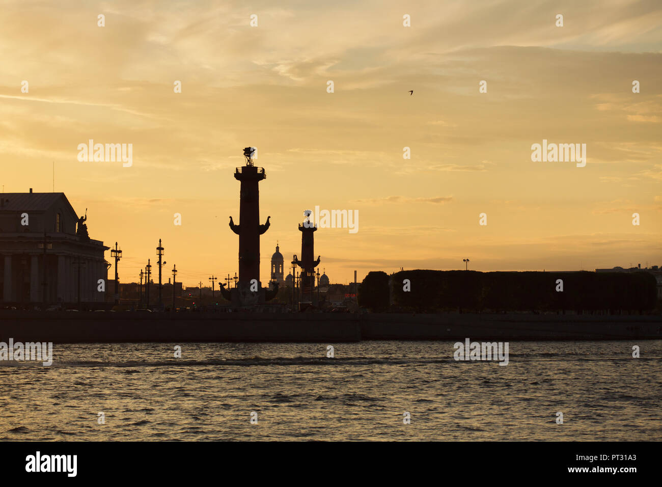 Rostral Columns designed by French neoclassical architect Jean-François Thomas de Thomon on the spit of Vasilievsky Island in Saint Petersburg, Russia, pictured at sunset. Saint Prince Vladimir's Cathedral in Petrogradsky District is seen in the background. Stock Photo