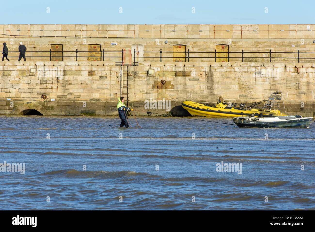 Workman in the water in Margate Harbour pulling a boat towards the