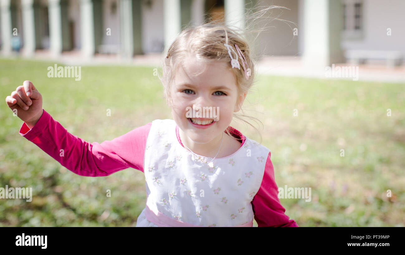 Little girl with blond hair and pink dress, laughing, approaching camera Stock Photo