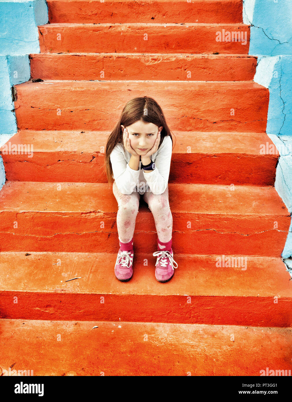 Unhappy 8 year old girl sitting on orange steps. Stock Photo