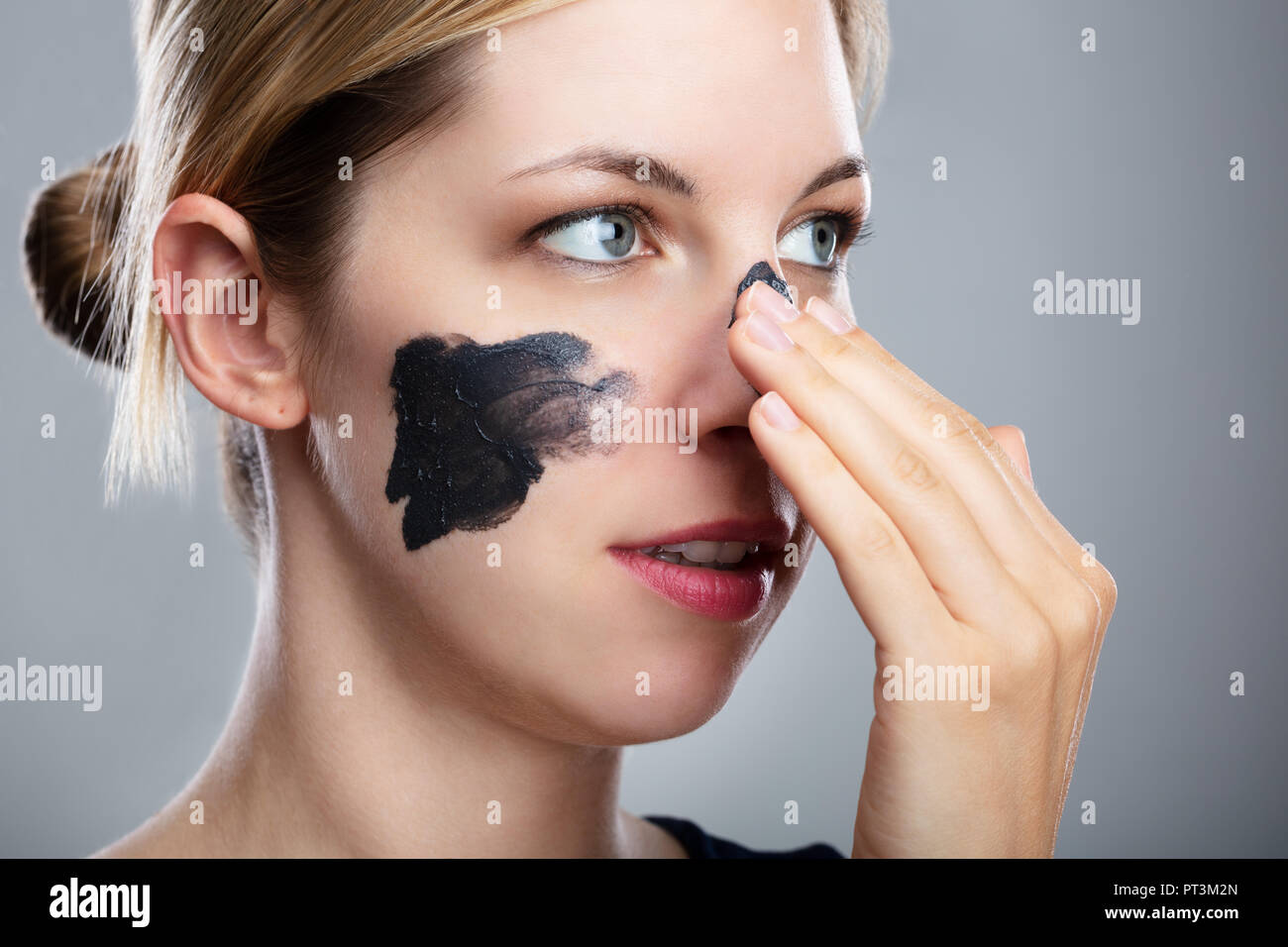 Portrait Of A Smiling Young Woman Applying Activated Charcoal Mask On Her Face Stock Photo